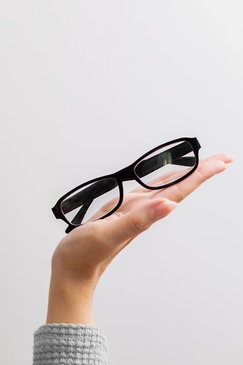 Hand holding a pair of black eyeglasses against a light gray background