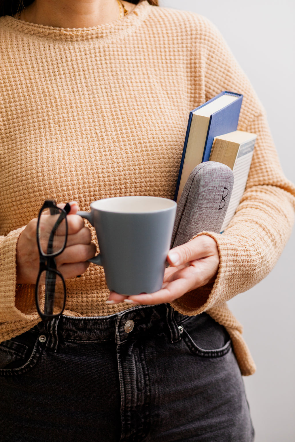 Person holding a mug and books with a neutral background