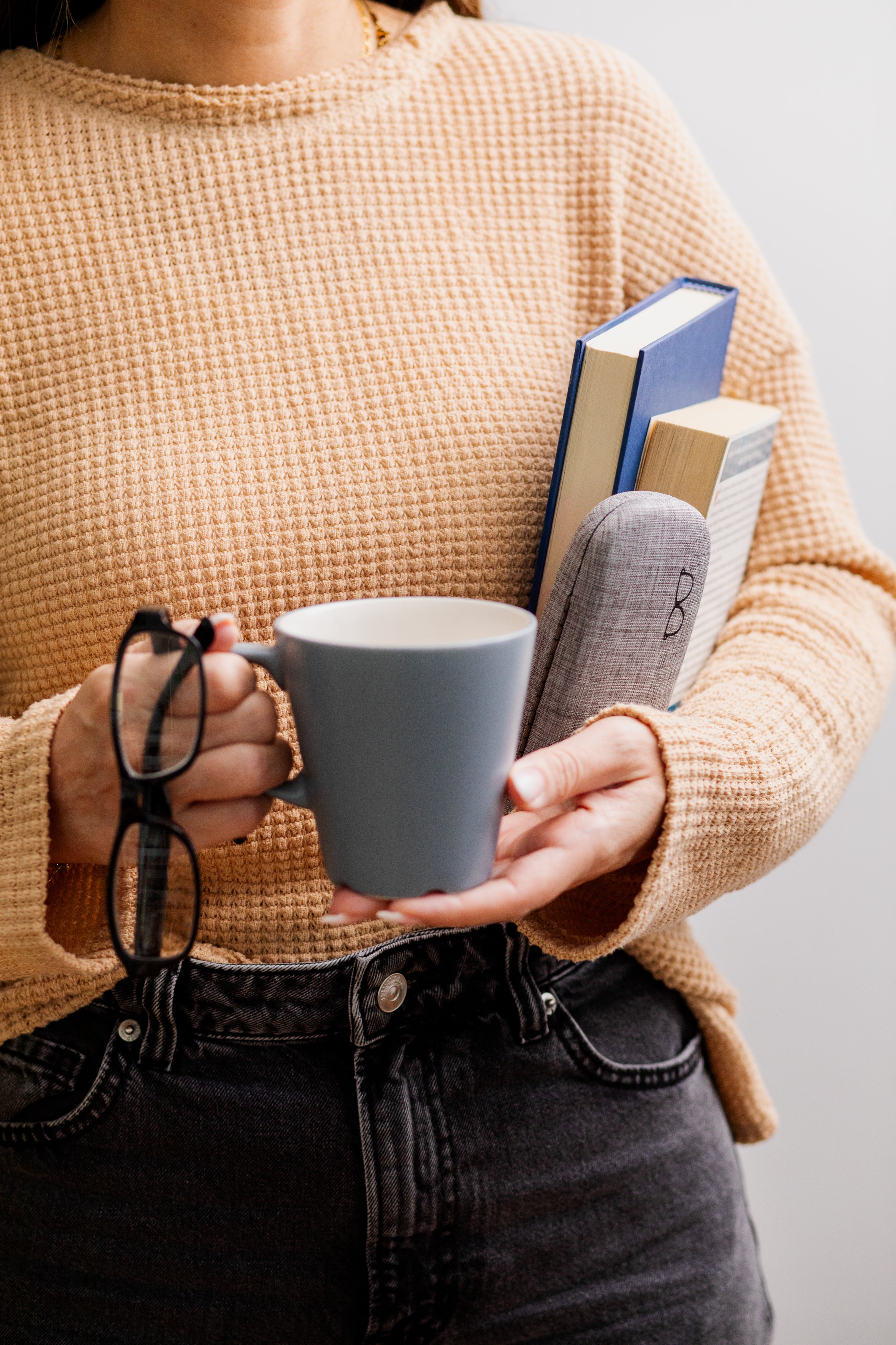 Person holding a mug and books with a neutral background