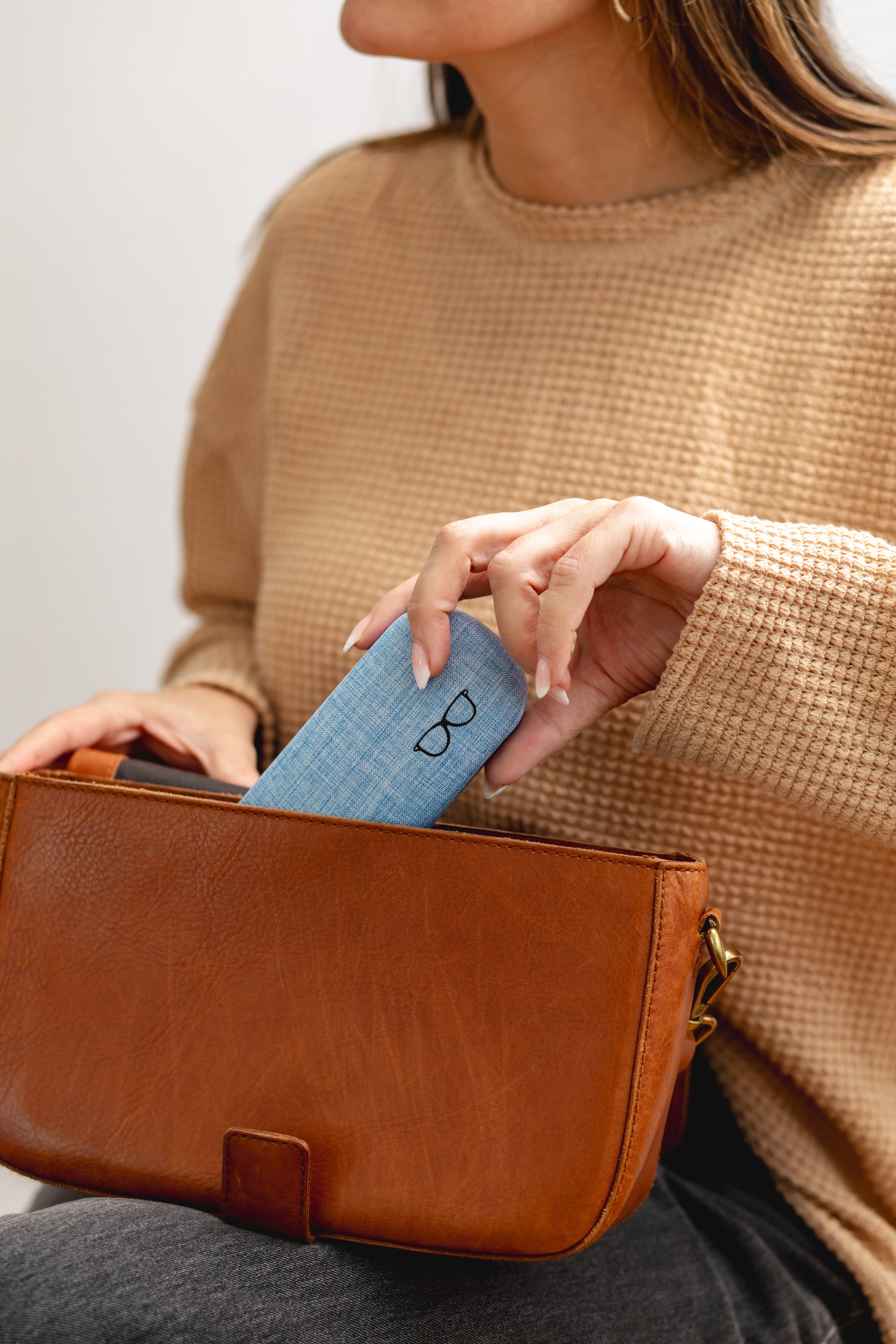 Person holding a brown leather bag and a blue card with glasses on it.