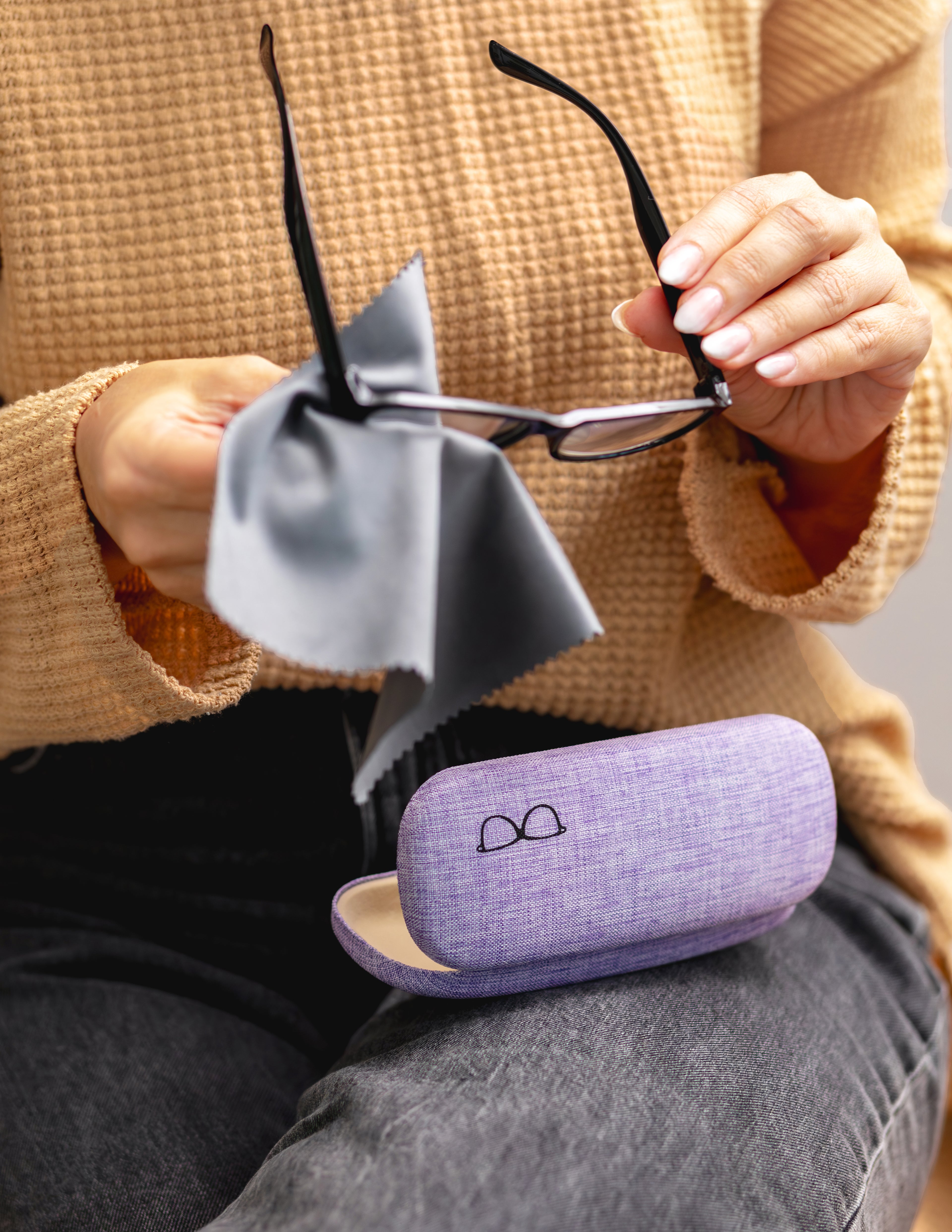 Person holding a pair of glasses with a purple case and gray cloth.