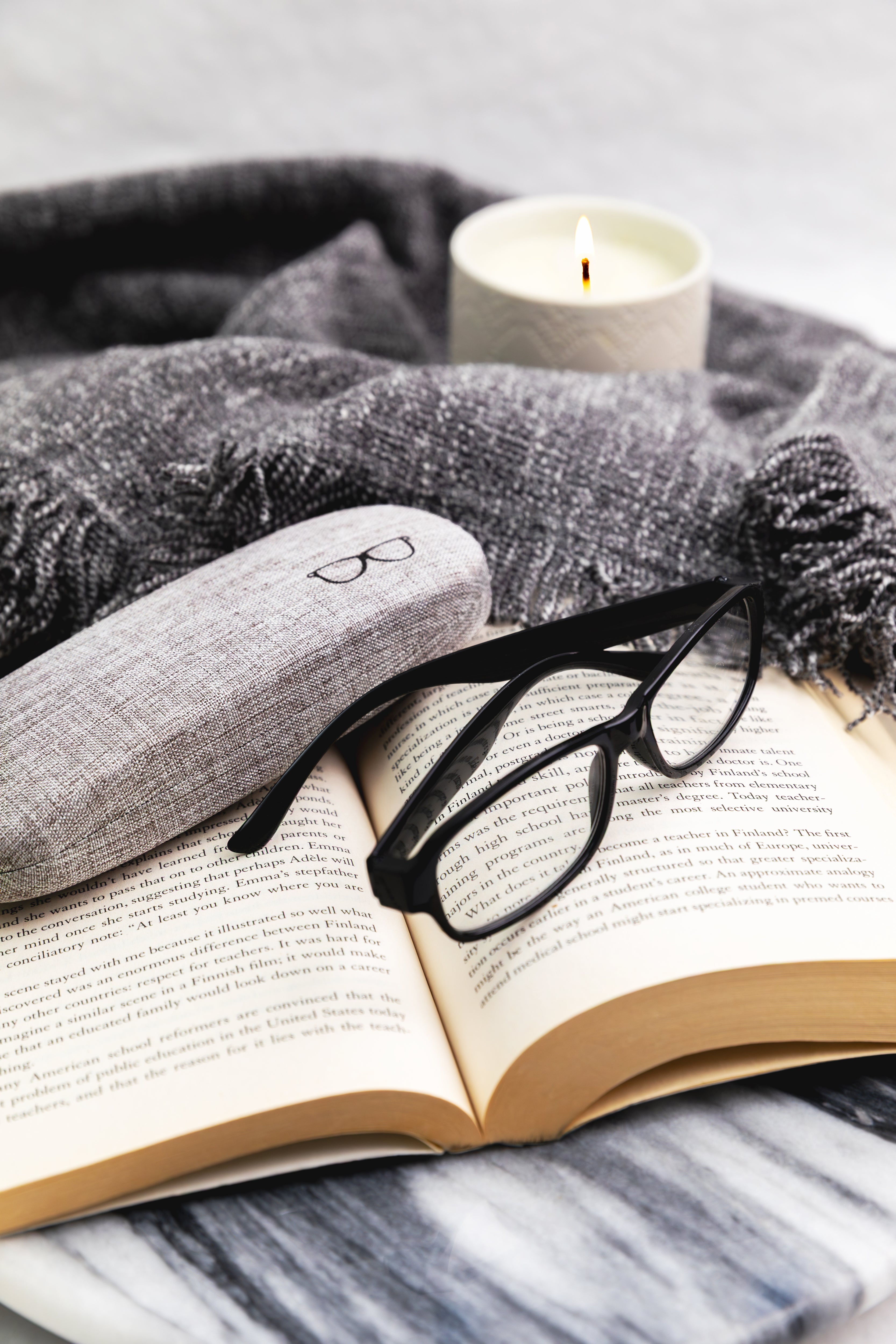 Open book with glasses, gray fabric, and a candle on a marble surface