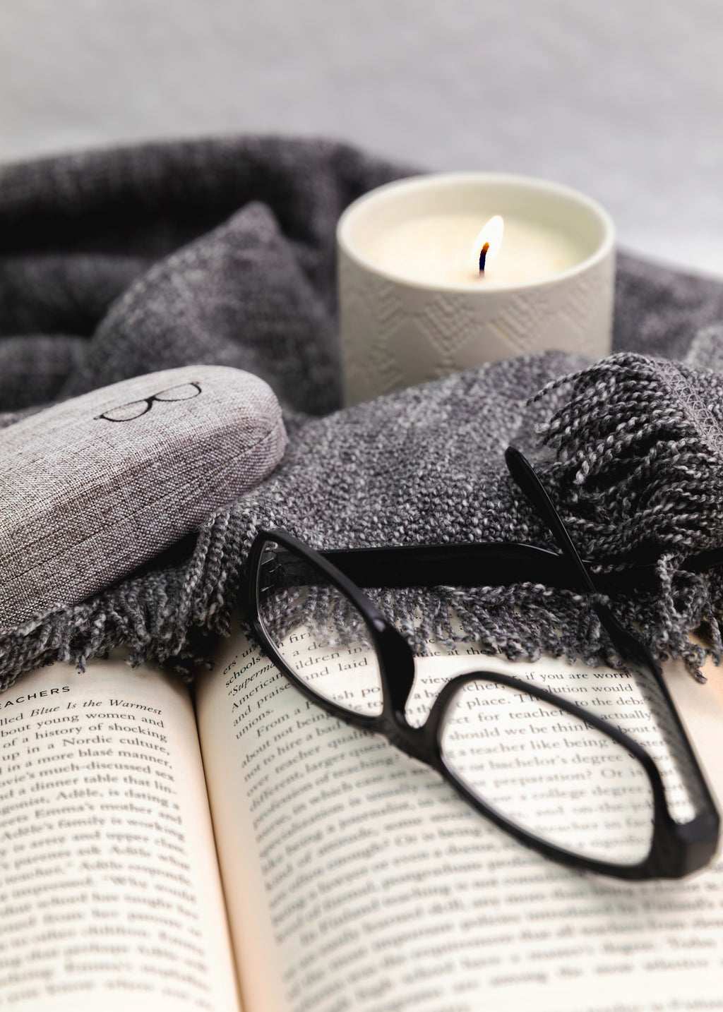 Open book with glasses, gray scarf, and candle on a gray background