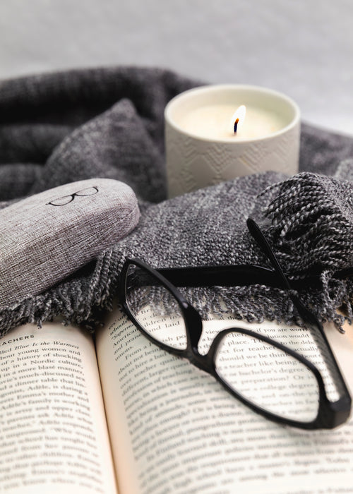 Open book with glasses, gray scarf, and candle on a gray background